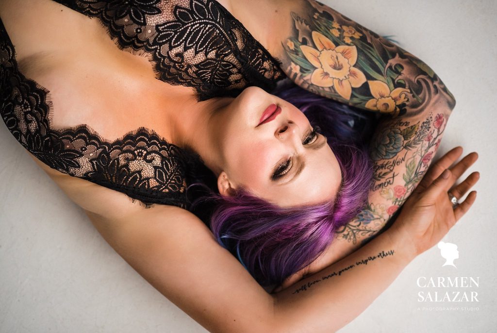 woman with colorful tattoos and purple and blue hair in black lacy lingerie with white background; Colorful and Artistic Boudoir Photography by Carmen Salazar