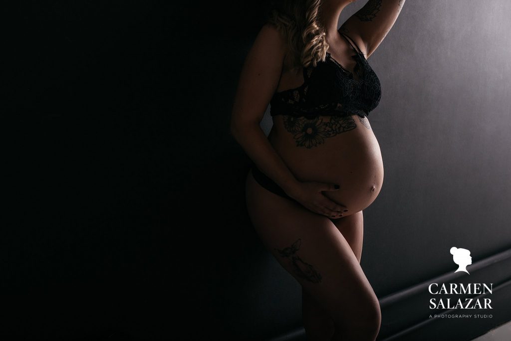 Expectant mother in black lingerie with black background. by Carmen Salazar