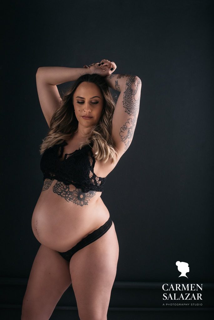 Woman in black lingerie set against black background; Maternity Boudoir Photography by Carmen Salazar