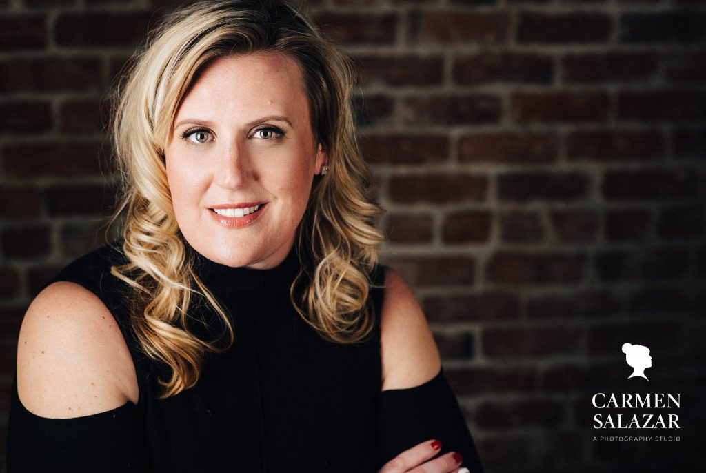 Woman in black shirt in front of brick wall, photography by Carmen Salazar