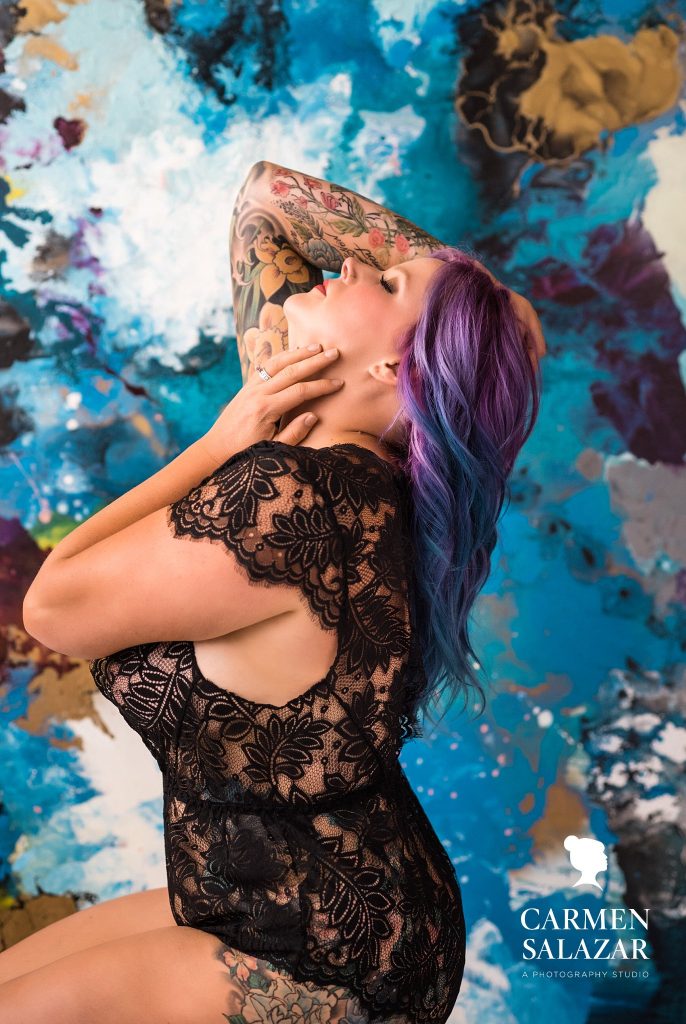 woman with colorful tattoos and purple and blue hair in black lacy lingerie with colorful background;  Boudoir Photography by Carmen Salazar 