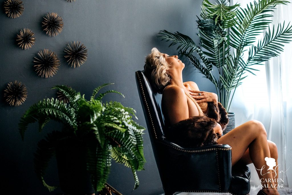 Woman in body jewelry and fur shawl sitting in a leather chair;  boudoir photography by Carmen Salazar