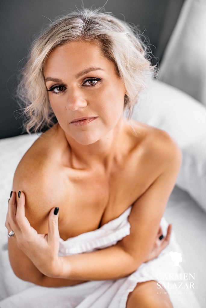 Blonde short haired woman between white sheets; boudoir photography by Carmen Salazar