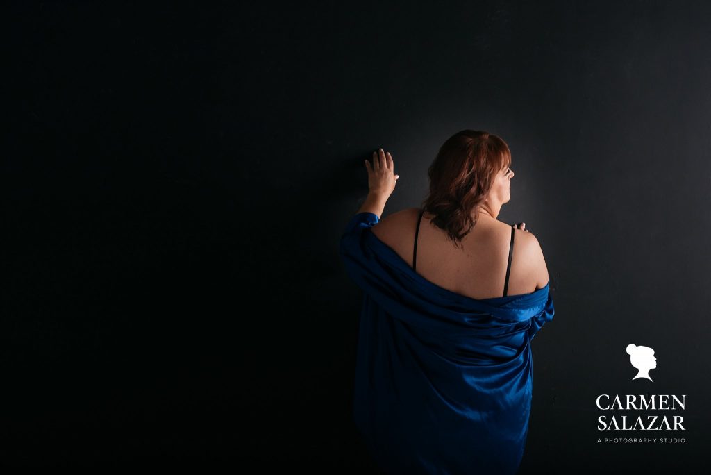 Woman in black bra and blue robe with a dark background.  Boudoir photography by Carmen Salazar