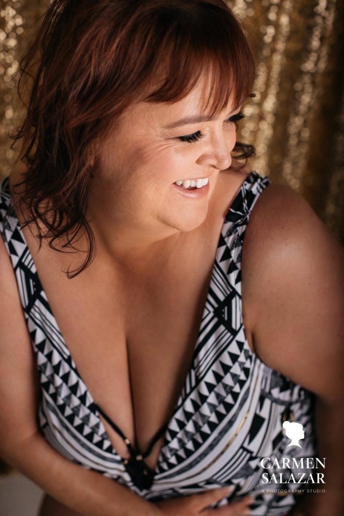 Woman in black and white graphic body suit in front of glittery gold curtains; boudoir photography by Carmen Salazar